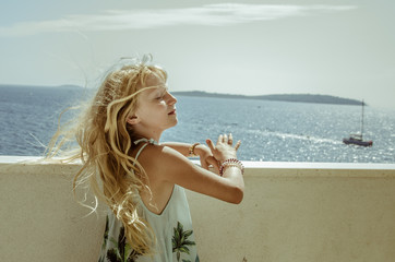 Fototapeta na wymiar adorable girl in windy weather with wavy long blond hair from blowing wind with in summer holiday atmosphere