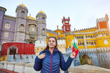 Obraz premium Young woman tourist walks in Pena Palace, Sintra holding the flag of Portugal in her hands. Travel and tourism in Europe