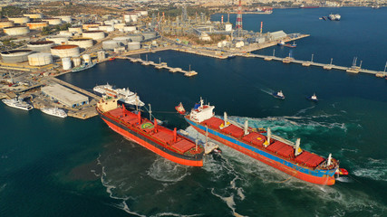 Obraz premium Aerial drone photo of industrial bulk carrier tanker being towed by tugboats in bay and shipyard of Elefsina, Attica, Greece