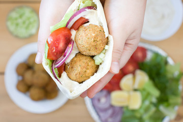 Falafel and fresh vegetables in pita bread in hands