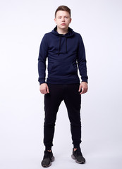 Naklejka premium Isolated portrait of handsome serious young man in black hoodie standing with his hands in pockets. Concept of hacking and fashion
