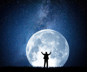 Silhouette of a man pulling his arms up on the background of the moon and the night starry sky. Elements of this image furnished by NASA.