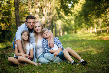 Naklejka na ściany i meble Happy family of four sitting on a grass in summer park outdoors and smiling