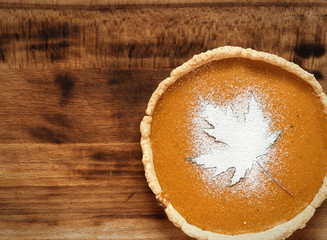 Homemade traditional American pumpkin pie on a wooden background. Decorated with powdered sugar in the form of a leaf . Top view. Copy space