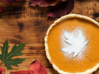 Homemade traditional American pumpkin pie on a black background. Decorated with powdered sugar in the form of a leaf and cranberries. Near autumn maple leaves. Top view. Copy space