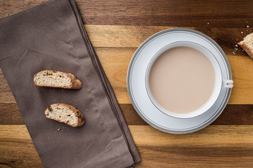up close cup of coffee with cream and biscotti on wooden table