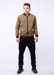 Young man in jeans, shiny nylon gold bomber jacket on white background.