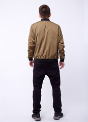 Naklejka premium Young man in jeans, shiny nylon gold bomber jacket on white background.