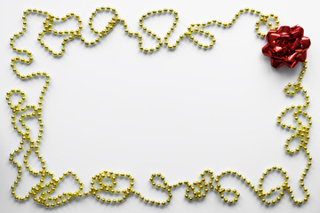 Festive frame arranged from gold chain and red bow. Copy space on white table for wish Merry Christmas.