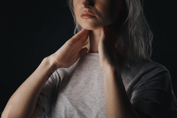 Female checking thyroid gland by herself. Close up of woman in white t- shirt touching neck with...