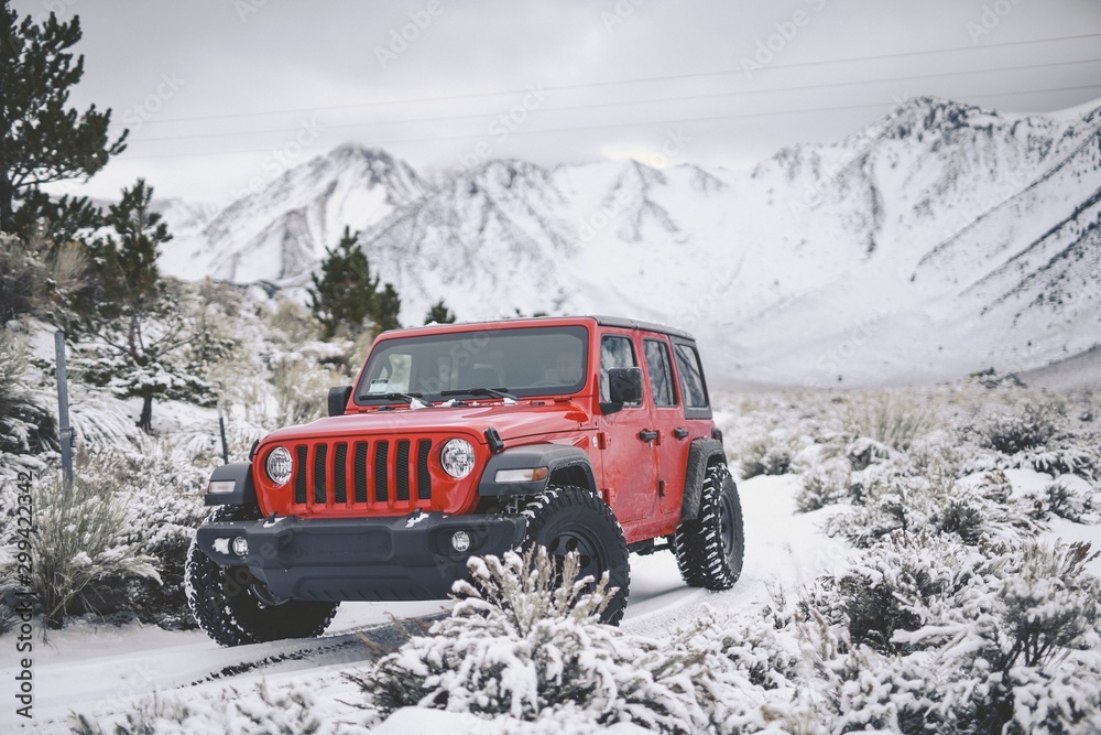 Poster beautiful shot of a red vehicle driving through a road covered with snow in the mountains