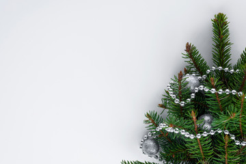 Top view of white table with little christmas tree branches with decorations such as silver baubles and chain. Copy space for greetings.