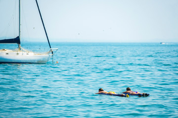 Garda, Italy - July, 06, 2019:  image of vacationers floating on air mattresses near parked motor boats