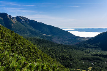 View of the ridge, green valley covered with forest. And in the distance the clouds above the lowlands forming the so-called sea of clouds.