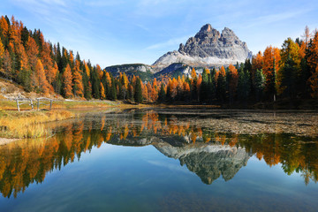 Lake with reflection of mountains at sunset in autumn, Dolomites, Italy. Landscape with Antorno lake, trees with orange leaves and high rocks in fall. Colorful forest
