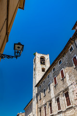 Fototapeta na wymiar The Palazzo del Podestà, in Piazza dei Priori in the ancient medieval village of Narni. The stone bell tower and the clock. Umbria, Terni, Italy. The blue sky on a summer day.
