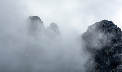 Man on top. Landscape of mountain peaks surrounded by clouds swirling next to them.