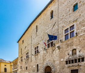 Fototapeta na wymiar Narni, Umbria, Italy - A large fountain in the center of the village of Narni. The old brick town hall building. Blue sky in the summer. The flag of Italy and the European Community (EEC