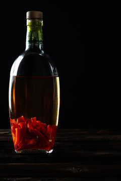 Sharp, Burning, Red Pepper Infused With Alcohol In A Transparent Bottle, Used For Medicinal Purposes, For Warming Up. Dark Photo, Vertical Arrangement.