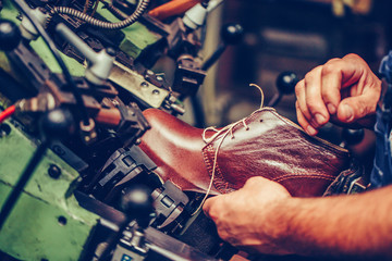 Experienced shoemaker using a special machine for putting shoes on the mold in the footwear industry.