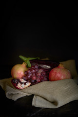 vertical eggplant and pomegranate still life with grape on sackcloth dark lighting