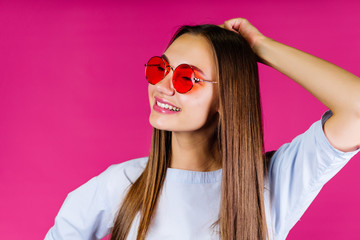 pink background. girl with a smile in glasses touches the back of her hand