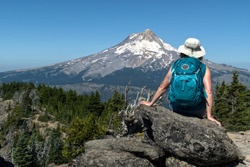 A mature woman hiker sites on a rock with her back to us and enjoys the view of Mt. Hood from...