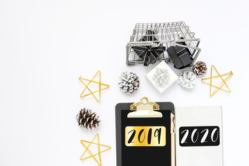 New year goals, golden stars, text 2019 2020 on black clipboard with paper blank, white, black gift boxes in shopping basket, pine cone. Motivation, inspiration concept, design flat lay, copy space