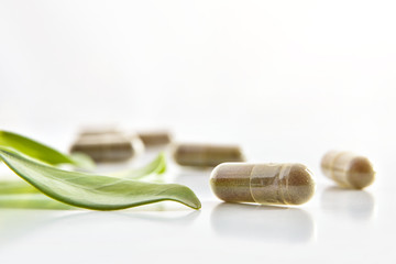 Natural medicine capsules and plant on white table isolated front