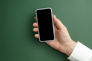 Male hand holding smartphone with empty screen on green background for text or design. Blank gadget...