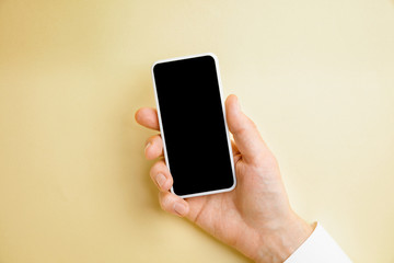 Fototapeta na wymiar Male hand holding smartphone with empty screen on yellow background for text or design. Blank gadget templates for contact or use in business. Finance, office, purchases. Mock up. Copyspace.