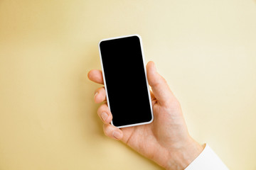 Male hand holding smartphone with empty screen on yellow background for text or design. Blank gadget templates for contact or use in business. Finance, office, purchases. Mock up. Copyspace.