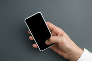 Male hand holding smartphone with empty screen on grey background for text or design. Blank gadget templates for contact or use in business. Finance, office, purchases. Mock up. Copyspace.