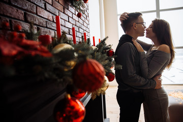 Loving couple hugs near the fireplace decorated with New Year decorations