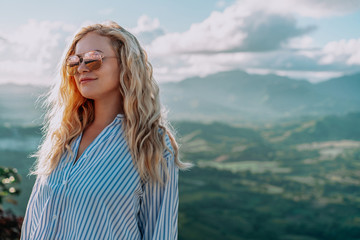 Beautiful view of young woman in sunglasses smiling on the top of the mountain on the dawn. Great landscape. Concept travel, dream