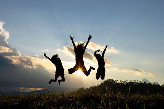 Silhouette group of happy children jumping playing on mountain at sunset, summer time