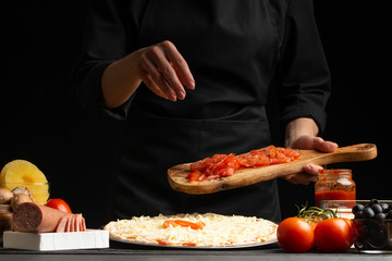 The chef cooks pizza, lays fresh tomatoes, on a background with ingredients. Recipe book, menu, home cooking.