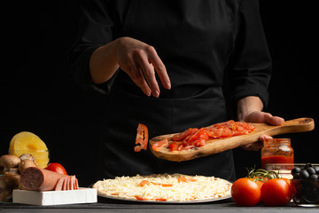 The chef cooks pizza, sprinkles fresh tomatoes, on a background with ingredients. Recipe book, menu, home cooking.