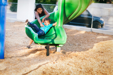 Older sister helping her younger brother go down a twisted slide in a kids playground.