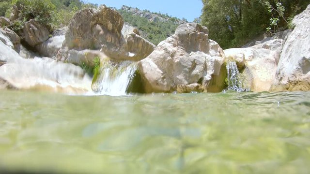Rocky stream with water flowing, moving camera over and under water surface, Spain, La Muga river, Catalonia