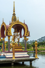 Ko Samui Island, Thailand - March 18, 2019: Wat Laem Suwannaram Chinese Buddhist Temple. Four headed Lord Brahma statue under gold-maroon baldachin. Hill, forest and housing in back. © Klodien