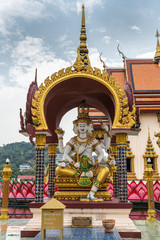 Ko Samui Island, Thailand - March 18, 2019: Wat Laem Suwannaram Chinese Buddhist Temple. Four headed Lord Brahma statue under gold-maroon baldachin. Hill, forest and housing in back. © Klodien