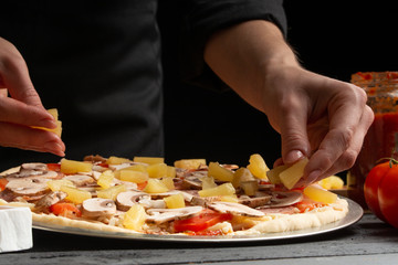 Chef cooks pizza, spreads sliced ​​pineapples, on a background with ingredients. Recipe book,...