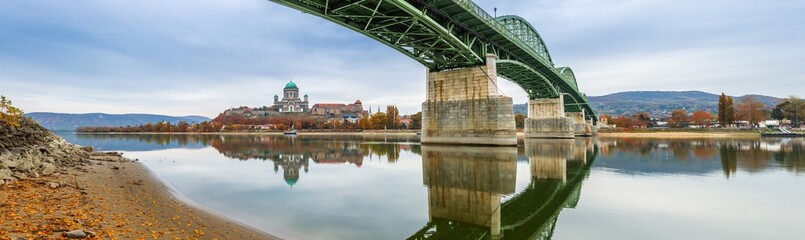 Esztergom, Hungary - Beautiful autumn morning with Maria Valeria Bridge and the Basilica of the Blessed Virgin Mary at Esztergom on a panoramic photo. Autumn colors and reflections on River Danube