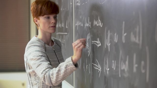 Young teacher lectures at the School of Mathematics, writes chalk on a blackboard