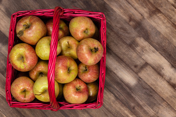 Organic fresh farm honey crisp apples photographed from above in a red wicker basket on a wooden table. Copy space.