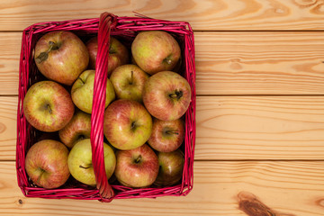 Organic fresh farm honey crisp apples photographed from above in a red wicker basket on a wooden table. Copy space.
