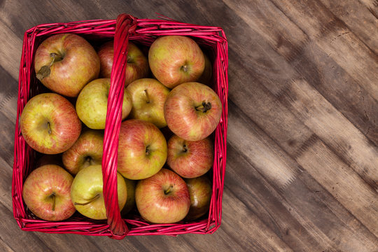 Organic fresh farm honey crisp apples photographed from above in a red wicker basket on a wooden table. Copy space.