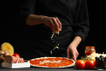 Chef cooks pizza, sprinkled with mozzarella cheese, freezing in motion on the background with ingredients. Recipe book, menu, home cooking