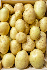 fresh potatoes in wooden box on wooden table, top view